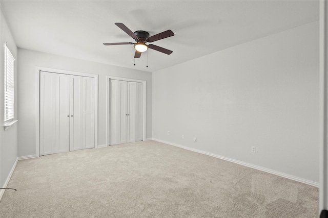 unfurnished bedroom with carpet floors, baseboards, a ceiling fan, and two closets