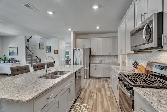 1409 Kirkdale Dr, Melissa, TX 75454 - kitchen featuring visible vents, appliances with stainless steel finishes, a sink, light stone counters, and light wood-style floors