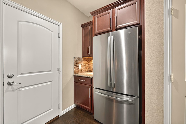 kitchen featuring dark wood-type flooring, tasteful backsplash, light stone countertops, and freestanding refrigerator