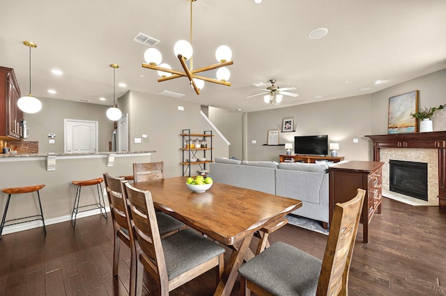 dining area featuring recessed lighting, dark wood finished floors, a glass covered fireplace, visible vents, and ceiling fan with notable chandelier