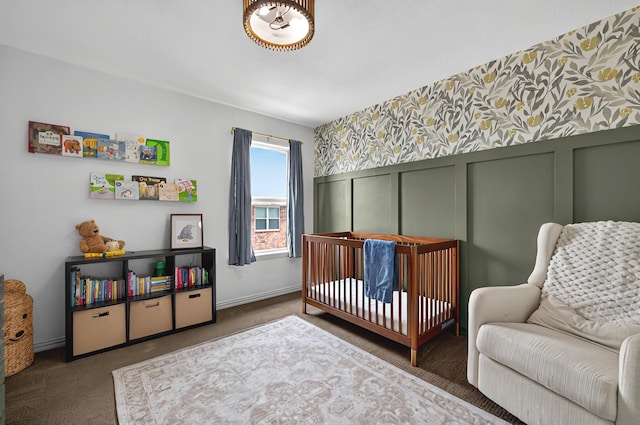 carpeted bedroom with a nursery area, baseboards, wallpapered walls, a decorative wall, and wainscoting