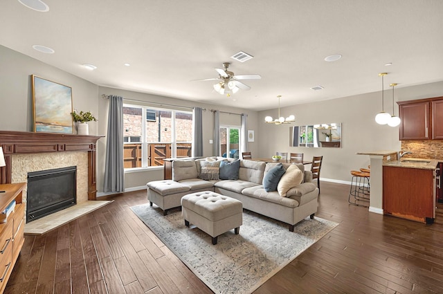 living room with ceiling fan with notable chandelier, a fireplace, baseboards, visible vents, and dark wood-type flooring