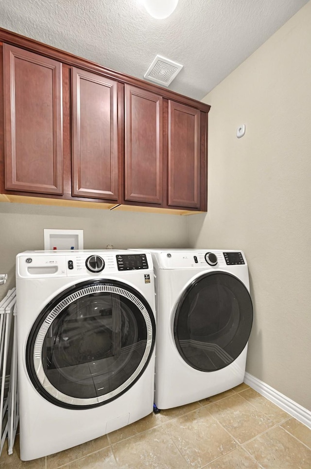 clothes washing area featuring a textured ceiling, washing machine and dryer, visible vents, baseboards, and cabinet space