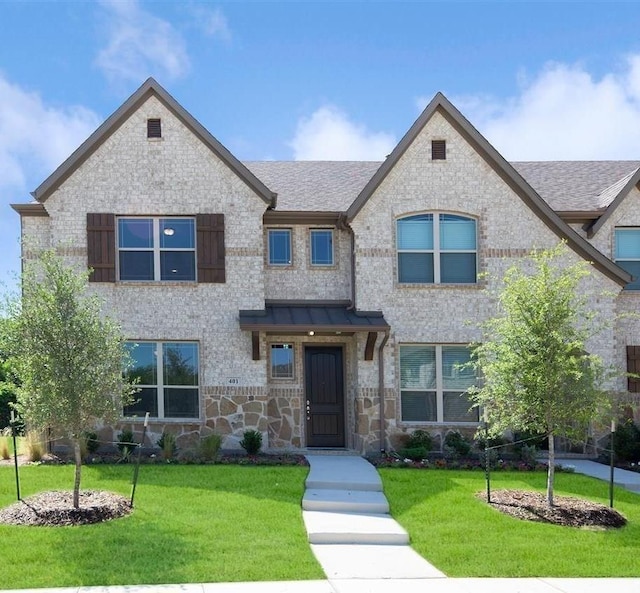 view of front of property with a shingled roof, a front yard, and stone siding