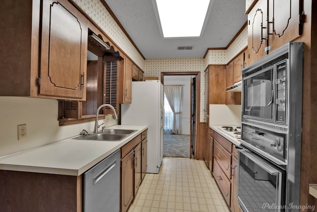 kitchen with a sink, stainless steel appliances, visible vents, light countertops, and wallpapered walls