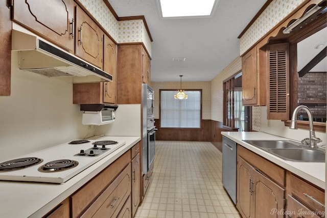 kitchen featuring wallpapered walls, appliances with stainless steel finishes, under cabinet range hood, light countertops, and a sink