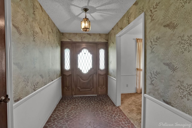 foyer featuring a textured ceiling, stone flooring, and wallpapered walls