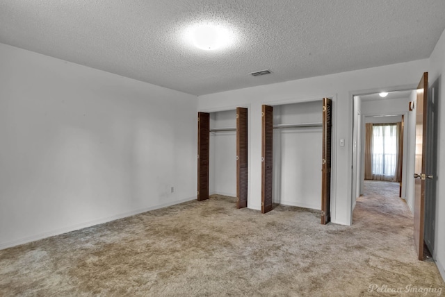 unfurnished bedroom featuring carpet flooring, a textured ceiling, visible vents, and multiple closets