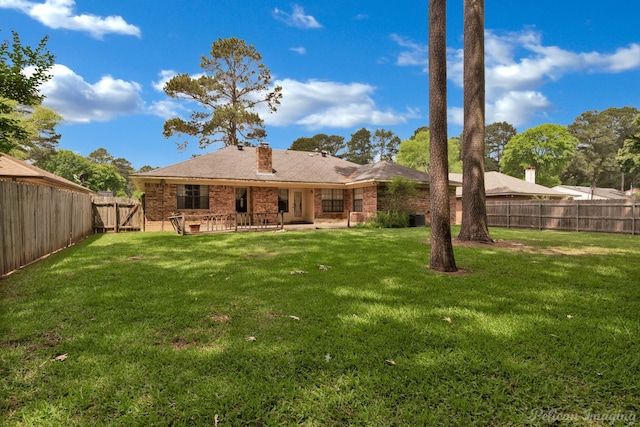 back of house with a yard, a chimney, a fenced backyard, and a patio area