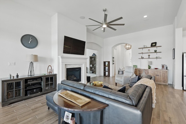 living room featuring a glass covered fireplace, wood finished floors, a ceiling fan, and arched walkways