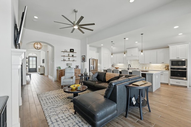living area featuring recessed lighting, arched walkways, ceiling fan, and light wood finished floors