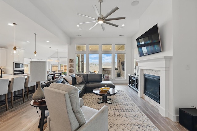 living room featuring light wood-type flooring, recessed lighting, ceiling fan, and a glass covered fireplace