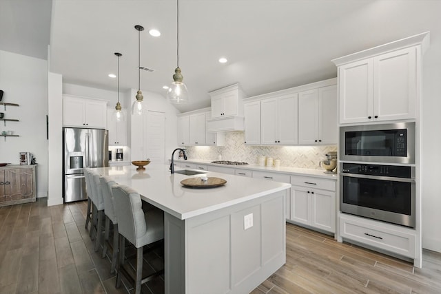 kitchen with decorative backsplash, a sink, stainless steel appliances, light countertops, and an island with sink