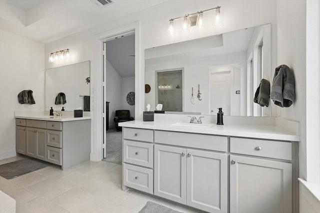 full bathroom with visible vents, two vanities, tiled shower, and a sink