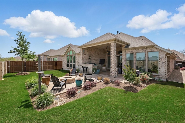 rear view of house with a yard, a fire pit, fence, brick siding, and a patio area