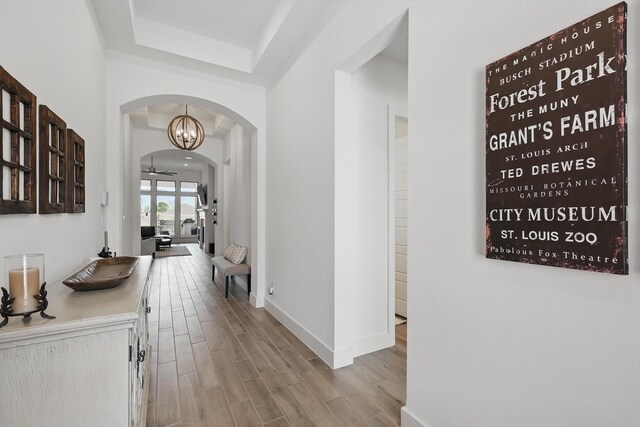 hallway featuring wood finished floors, baseboards, and arched walkways