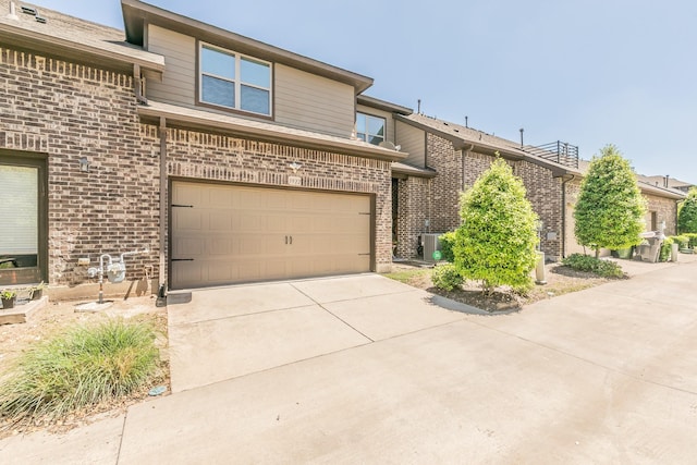 view of front facade featuring cooling unit, concrete driveway, an attached garage, and brick siding