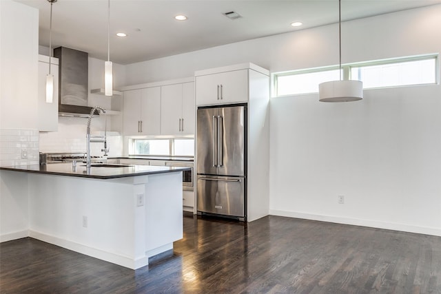 kitchen with wall chimney range hood, plenty of natural light, wall oven, high end fridge, and decorative light fixtures