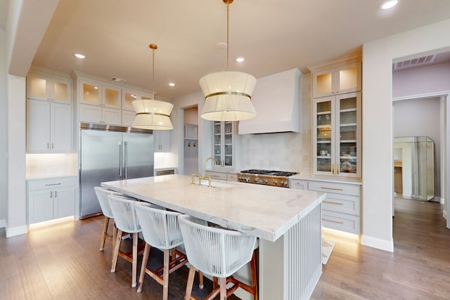 kitchen featuring backsplash, built in fridge, custom exhaust hood, light wood finished floors, and recessed lighting