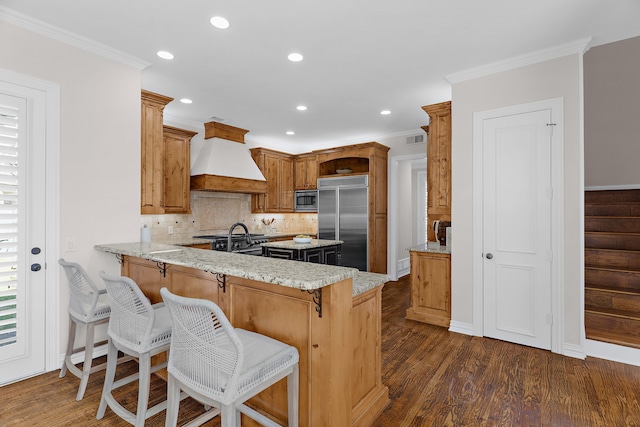 kitchen featuring built in appliances, ornamental molding, a peninsula, and premium range hood
