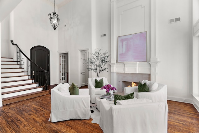 living area with stairway, visible vents, baseboards, a towering ceiling, and wood finished floors