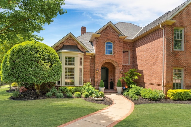 traditional home featuring roof with shingles, a chimney, a front yard, and brick siding