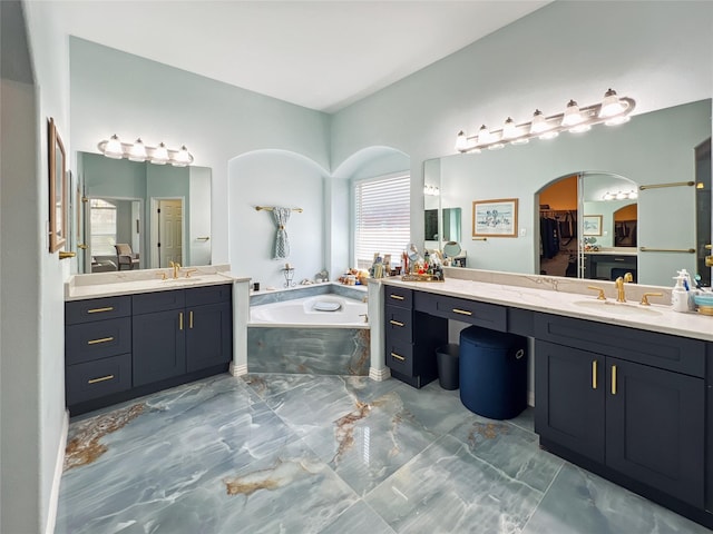 full bath with two vanities, a bath, marble finish floor, and a sink