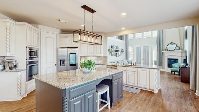 139 Townlake Dr, Prosper, TX 75078 - kitchen with stainless steel appliances, a sink, a glass covered fireplace, a center island, and light wood finished floors