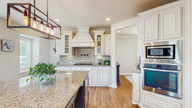 139 Townlake Dr, Prosper, TX 75078 - kitchen with appliances with stainless steel finishes, custom range hood, light stone countertops, light wood-style flooring, and tasteful backsplash
