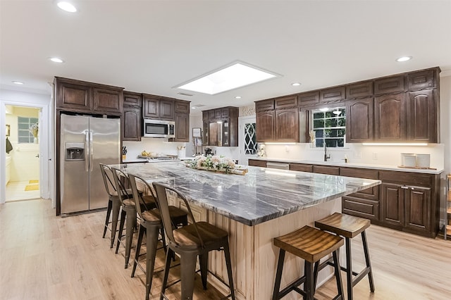 kitchen with appliances with stainless steel finishes, light wood-style floors, dark brown cabinetry, and a skylight