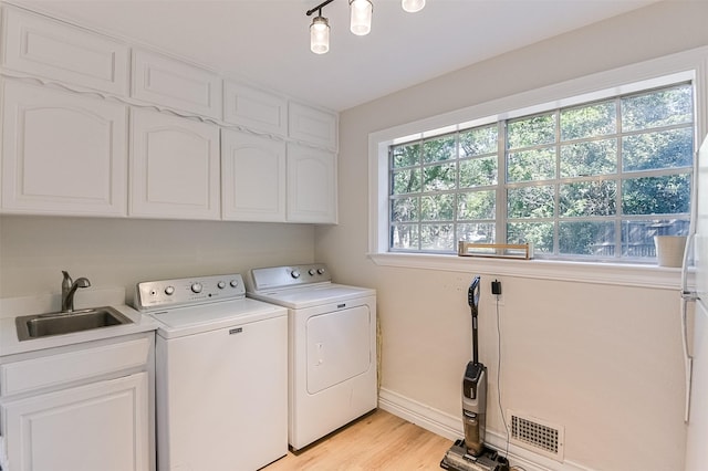 washroom featuring washer and dryer, cabinet space, light wood-type flooring, a sink, and visible vents
