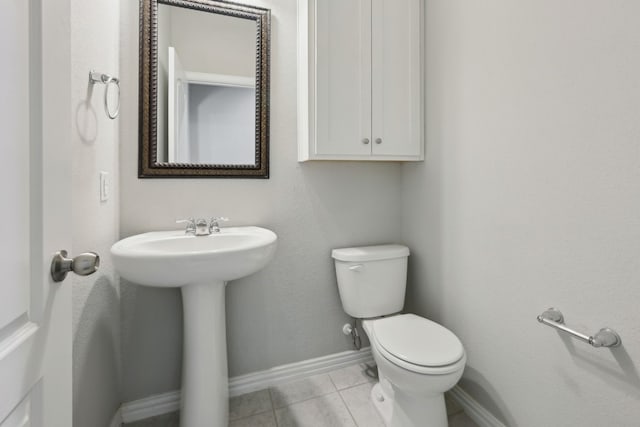 half bathroom featuring a sink, toilet, tile patterned flooring, and baseboards