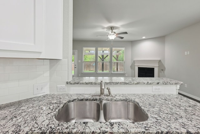 kitchen featuring light stone countertops, decorative backsplash, white cabinets, ceiling fan, and a sink