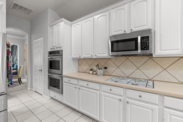 2209 Graystone Ct, Keller, TX 76248 - kitchen with appliances with stainless steel finishes, arched walkways, tasteful backsplash, light countertops, and white cabinetry