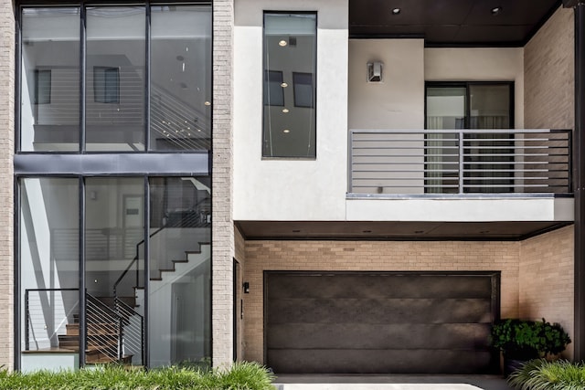entrance to property with a garage, brick siding, stucco siding, and a balcony