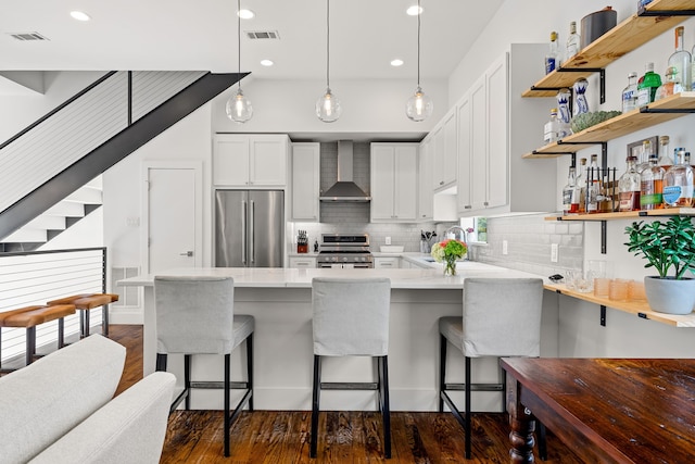 kitchen featuring a peninsula, stainless steel appliances, visible vents, wall chimney exhaust hood, and dark wood-type flooring