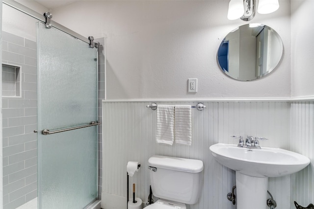 bathroom featuring toilet, a sink, a shower stall, and wainscoting