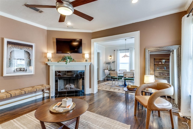 living room with ornamental molding, a tile fireplace, a ceiling fan, and wood finished floors