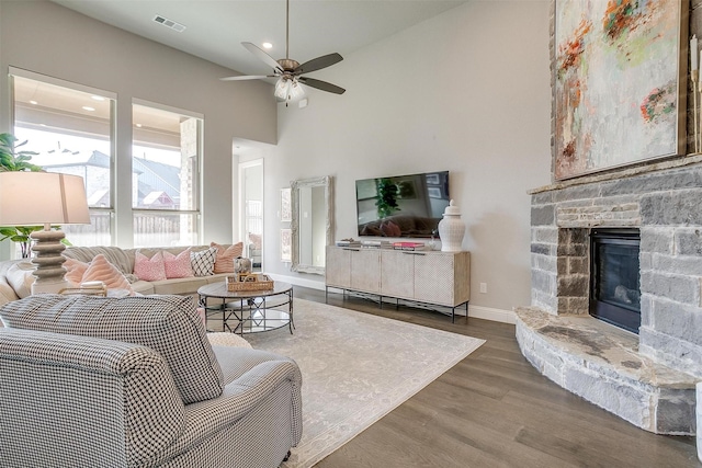living area featuring wood finished floors, a stone fireplace, baseboards, visible vents, and a ceiling fan