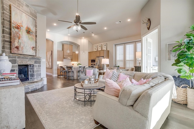 living room featuring a fireplace, a ceiling fan, visible vents, arched walkways, and wood finished floors