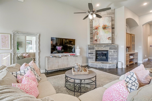 living room featuring baseboards, arched walkways, recessed lighting, wood finished floors, and a stone fireplace
