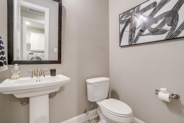 half bath featuring visible vents, toilet, washer / clothes dryer, and baseboards