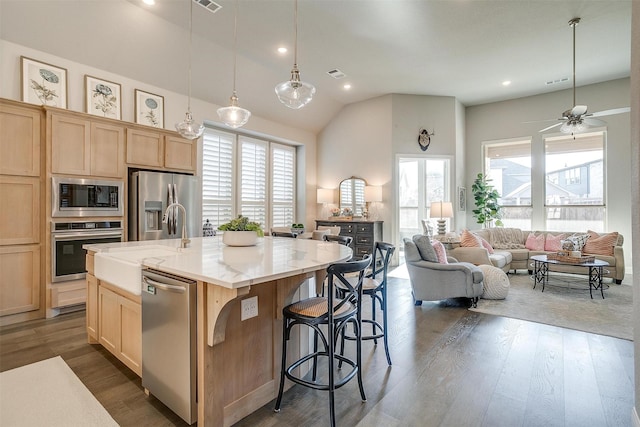 kitchen featuring light brown cabinetry, stainless steel appliances, dark wood finished floors, and an island with sink