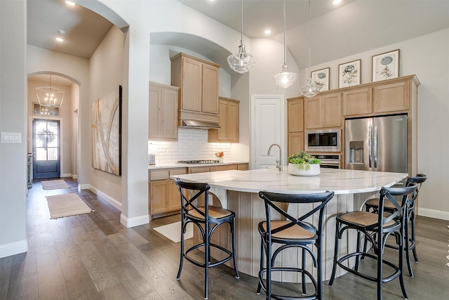 kitchen featuring stainless steel appliances, baseboards, light brown cabinetry, arched walkways, and backsplash