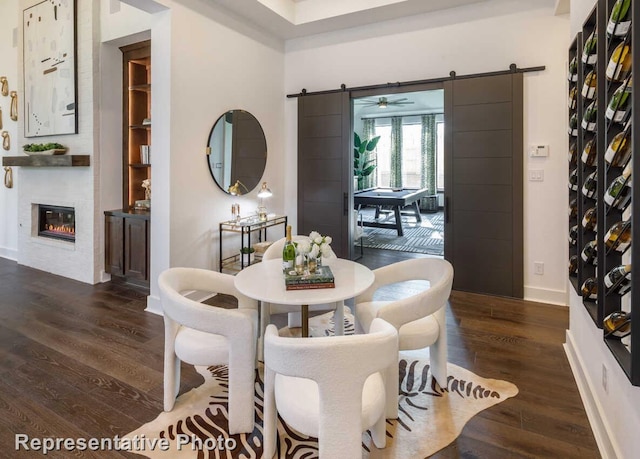 dining room featuring baseboards, a barn door, wood finished floors, and a glass covered fireplace