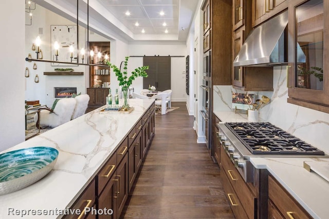 kitchen with light stone counters, glass insert cabinets, stainless steel gas stovetop, under cabinet range hood, and dark wood-style flooring