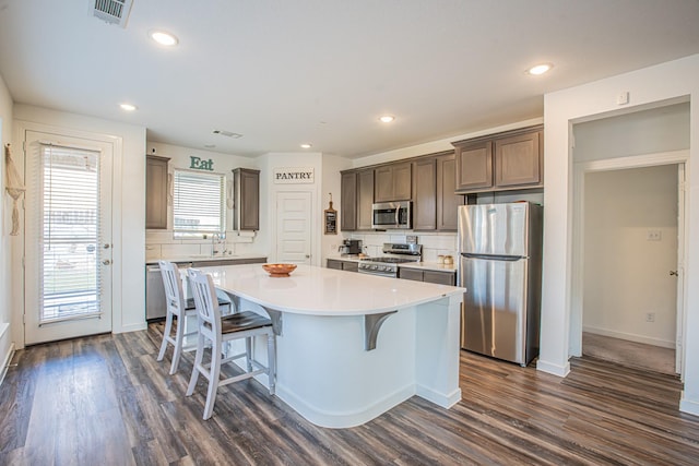 kitchen with decorative backsplash, dark wood-type flooring, a breakfast bar, a kitchen island, and appliances with stainless steel finishes