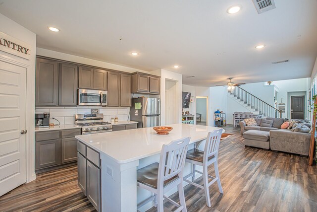 kitchen with appliances with stainless steel finishes, visible vents, a kitchen island, a kitchen bar, and dark wood-type flooring
