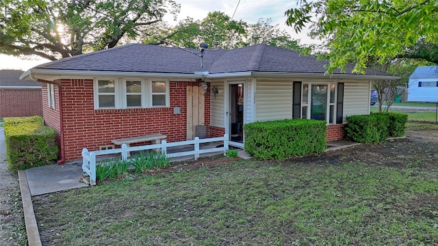 ranch-style home with a front yard, a shingled roof, and brick siding