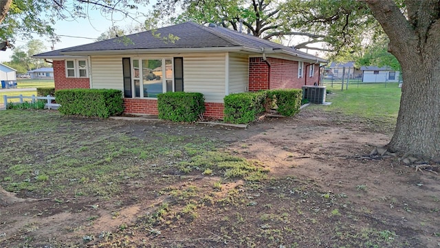 view of home's exterior featuring brick siding, fence, a shingled roof, central air condition unit, and a lawn